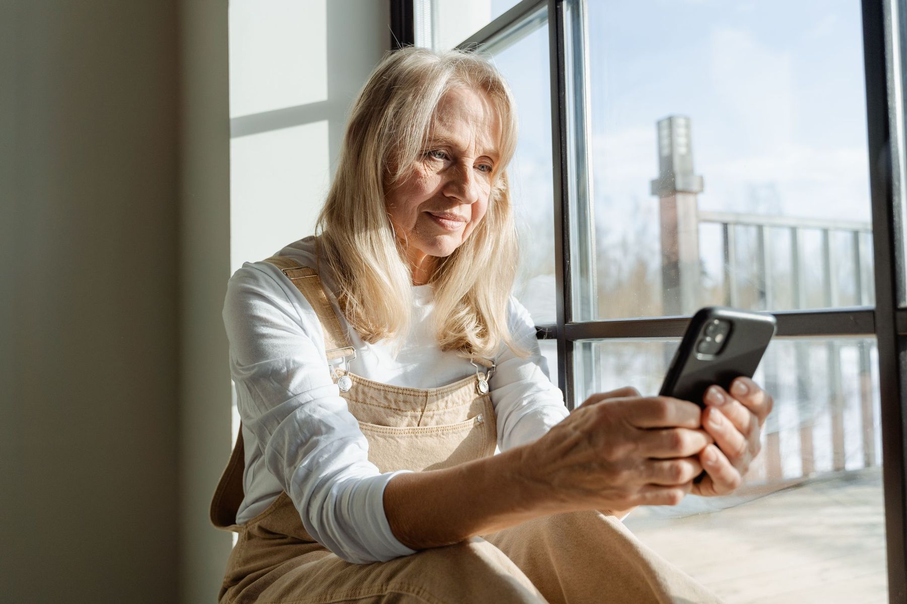 A woman smiling at a text on her phone by a sunny window