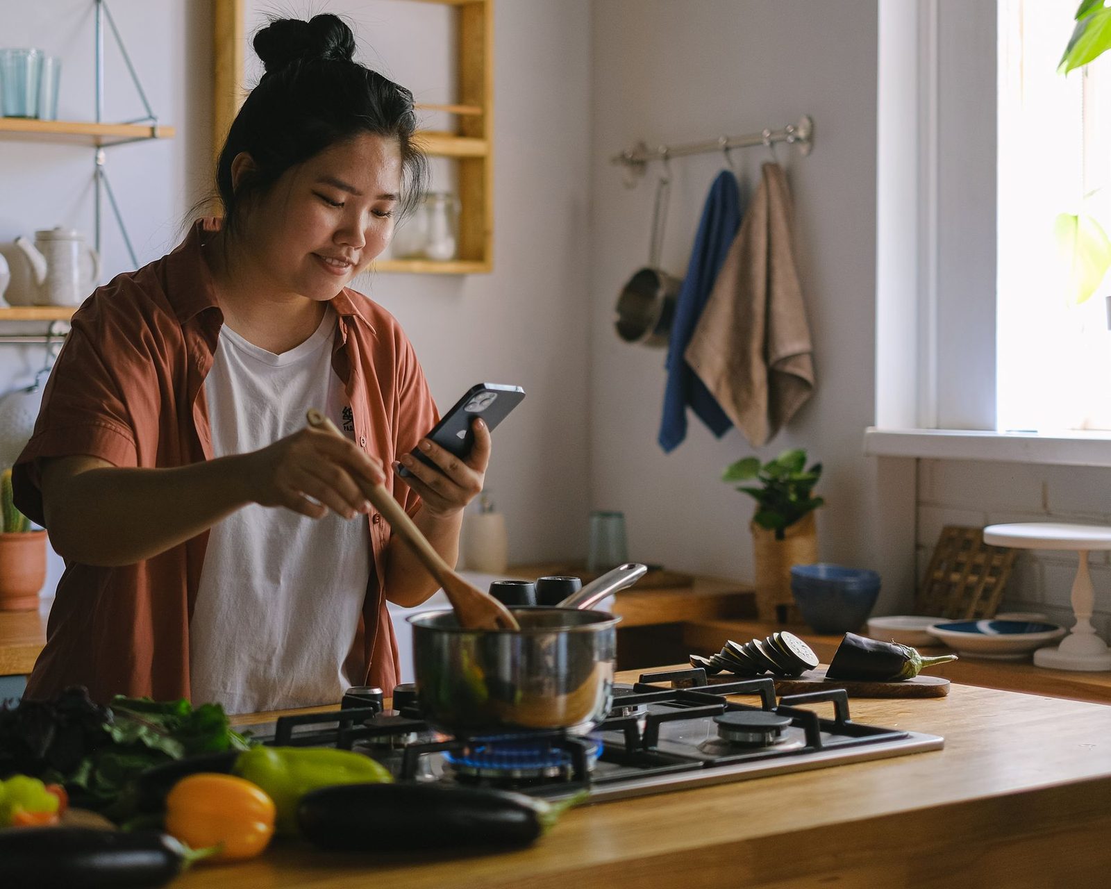 A woman checking a text on her phone while she cooks dinner